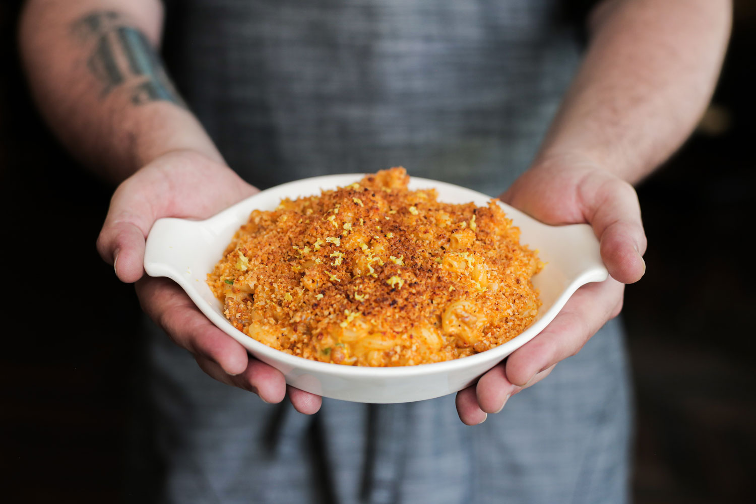 chef in apron holding white ceramic platter filled with mac and cheese dish